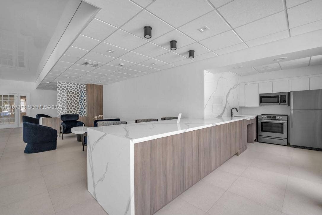 1800 N Andrews Avenue, #9K, Fort Lauderdale, Fort Lauderdale, FL 33311 Large kitchen island featuring waterfall-edge composite stone countertops and wood-finish cabinetry, accented by stone slab backsplashes and stainless steel appliances
