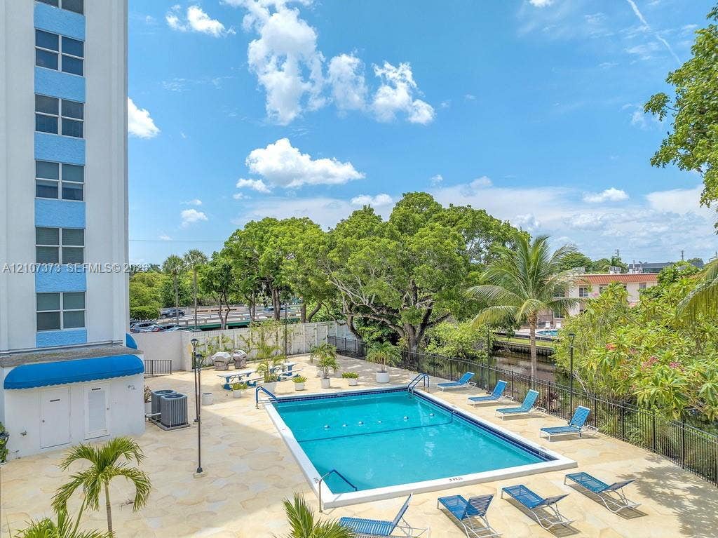 1800 N Andrews Avenue, #9K, Fort Lauderdale, Fort Lauderdale, FL 33311 Rectangular swimming pool with light-toned stone decking, enclosed by metal fencing and surrounded by mature trees and palm foliage