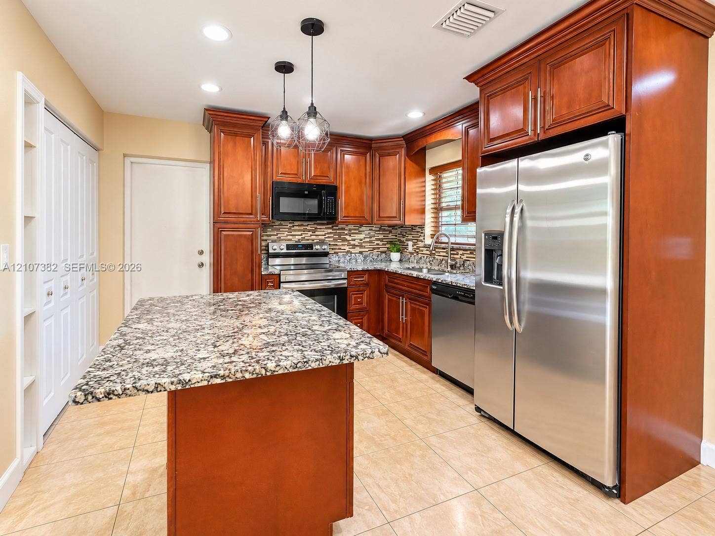 859 Caroline Circle, Palm Beach, FL 33413 Kitchen featuring stained wood cabinetry, stone countertops, a central island, tile flooring, and stainless steel appliances