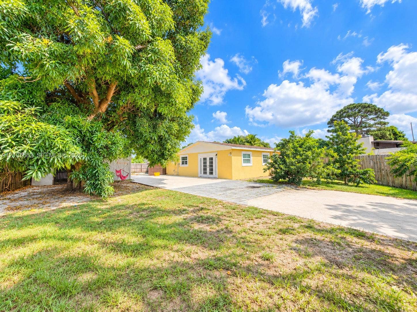 859 Caroline Circle, Palm Beach, FL 33413 Rear exterior featuring a stucco facade, double glass panel doors, concrete paver patio, and mature tree canopy