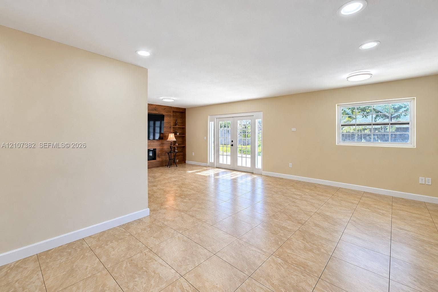 859 Caroline Circle, Palm Beach, FL 33413 Neutral tile flooring, recessed lighting, double French doors, and a wood-paneled accent wall with a built-in fireplace