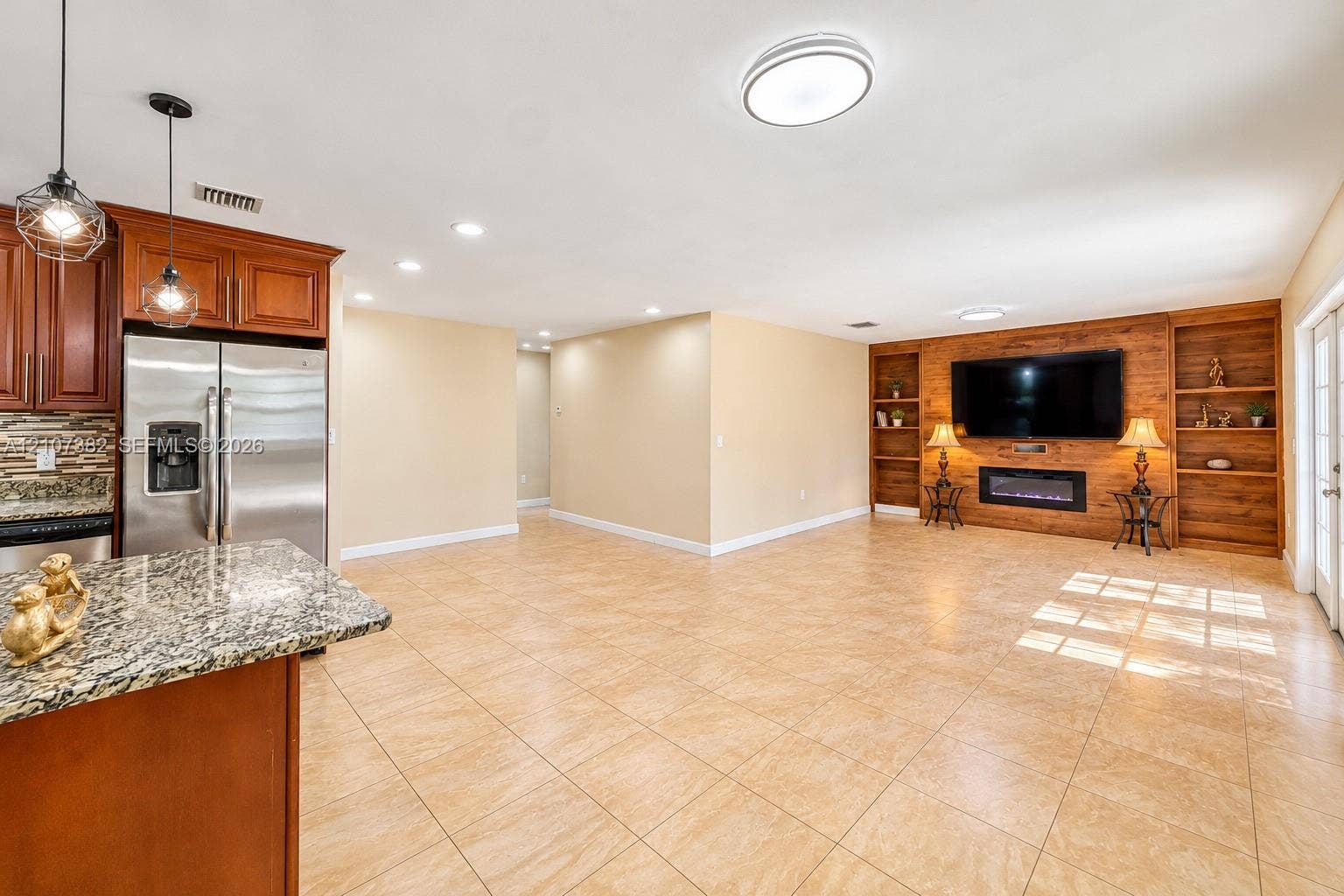 859 Caroline Circle, Palm Beach, FL 33413 Open kitchen featuring stone countertops, custom wood cabinetry, and stainless steel appliances, anchored by a living area with a wood-paneled accent wall, built-in shelving, and an electric fireplace