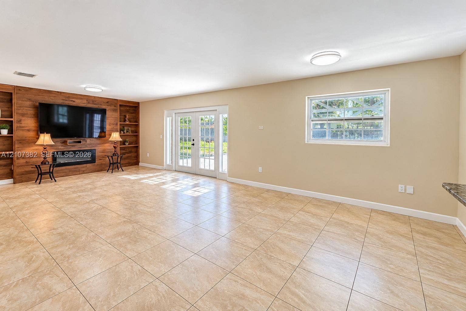 859 Caroline Circle, Palm Beach, FL 33413 Spacious interior featuring large-format tile flooring, built-in wood-finish cabinetry, a sleek electric fireplace, and double-pane French doors