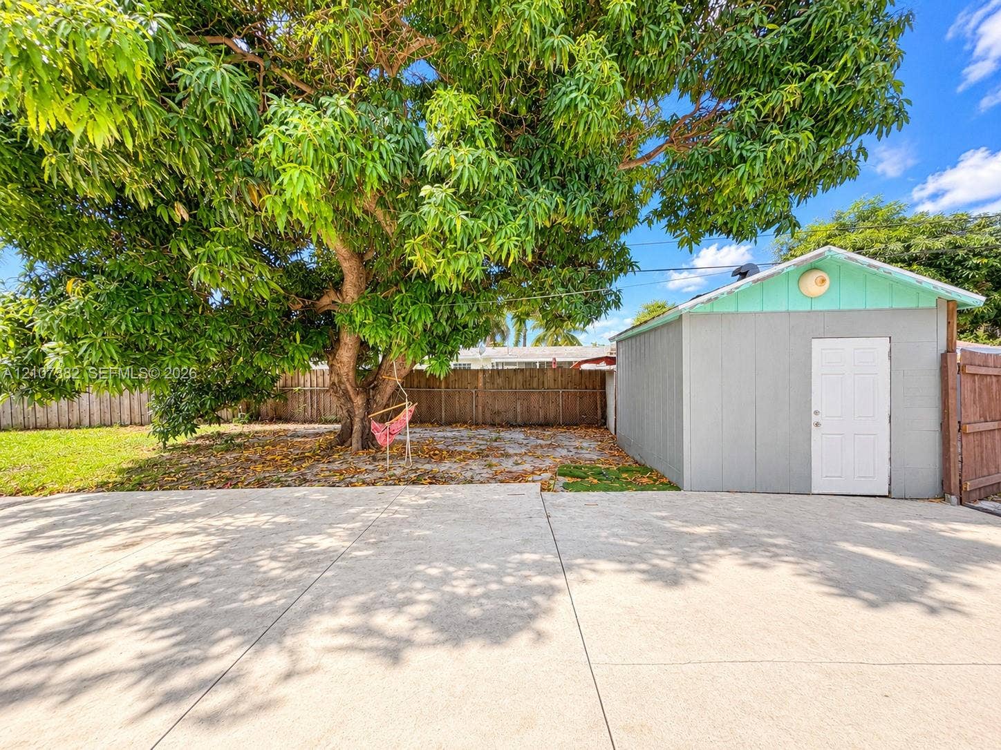 859 Caroline Circle, Palm Beach, FL 33413 Expansive concrete paved area, detached storage structure with white door, mature tree, and full-height wood fencing