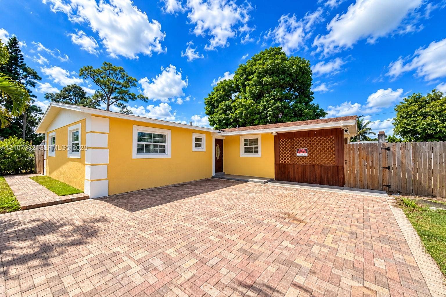 859 Caroline Circle, Palm Beach, FL 33413 Stucco exterior featuring corner quoins, expansive paver driveway, integrated wooden lattice screen, and wood-paneled privacy fencing