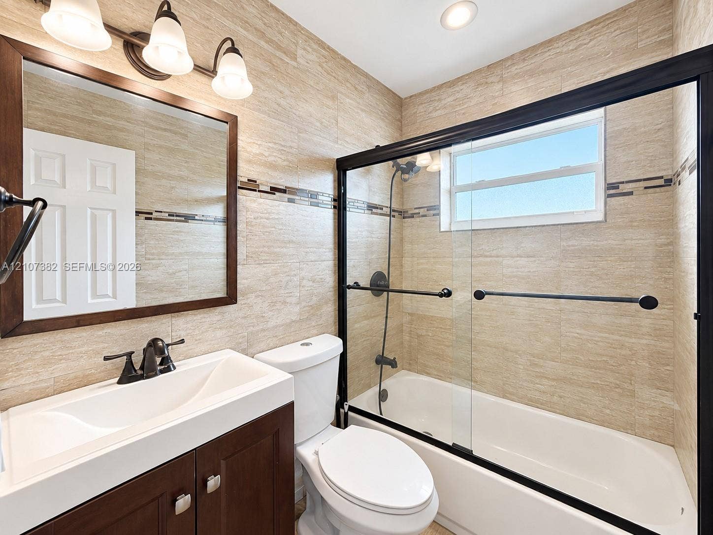 859 Caroline Circle, Palm Beach, FL 33413 Bathroom featuring full-wall textured tiling, dark wood-finish vanity with a rectangular sink, sliding glass shower door with matte black frame, and coordinated matte black fixtures
