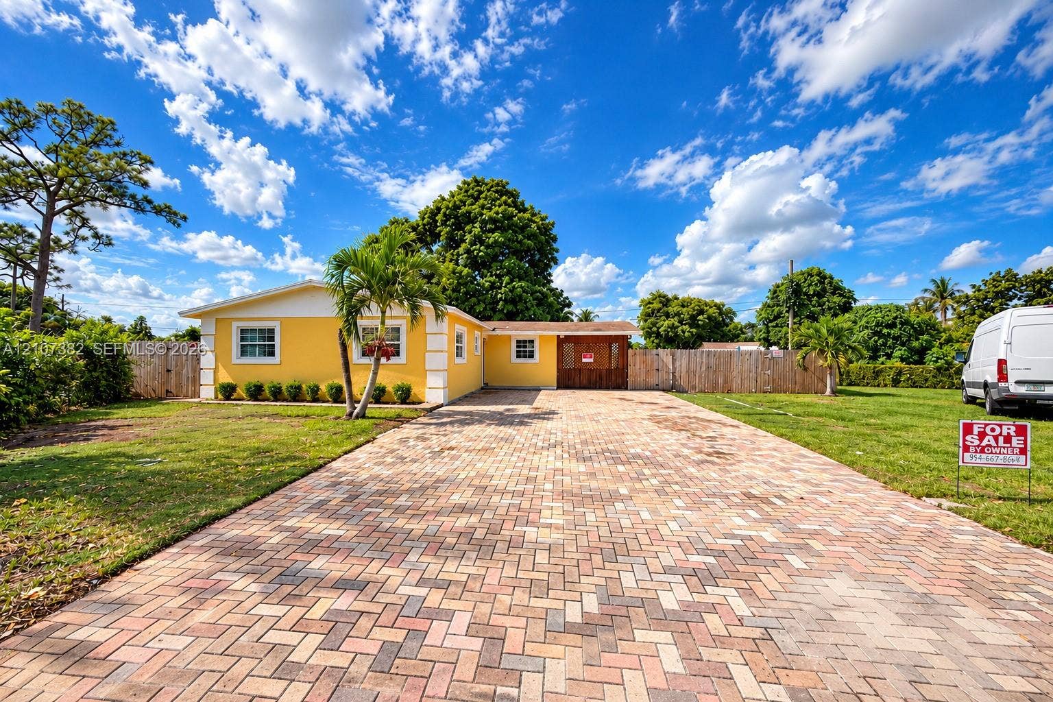 859 Caroline Circle, Palm Beach, FL 33413 Exterior featuring a multi-tone herringbone paver driveway, yellow stucco facade, white trim accents, and perimeter wood privacy fencing