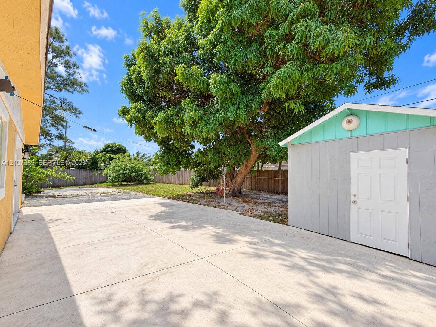 859 Caroline Circle, Palm Beach, FL 33413 Spacious concrete patio featuring a detached storage structure and a mature canopy tree within a fenced backyard