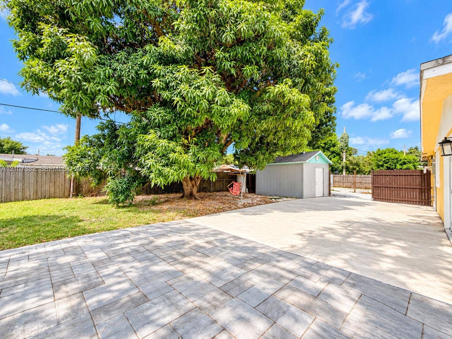 859 Caroline Circle, Palm Beach, FL 33413 Rear yard featuring a paved patio, large mature tree, detached storage structure, and fenced perimeter