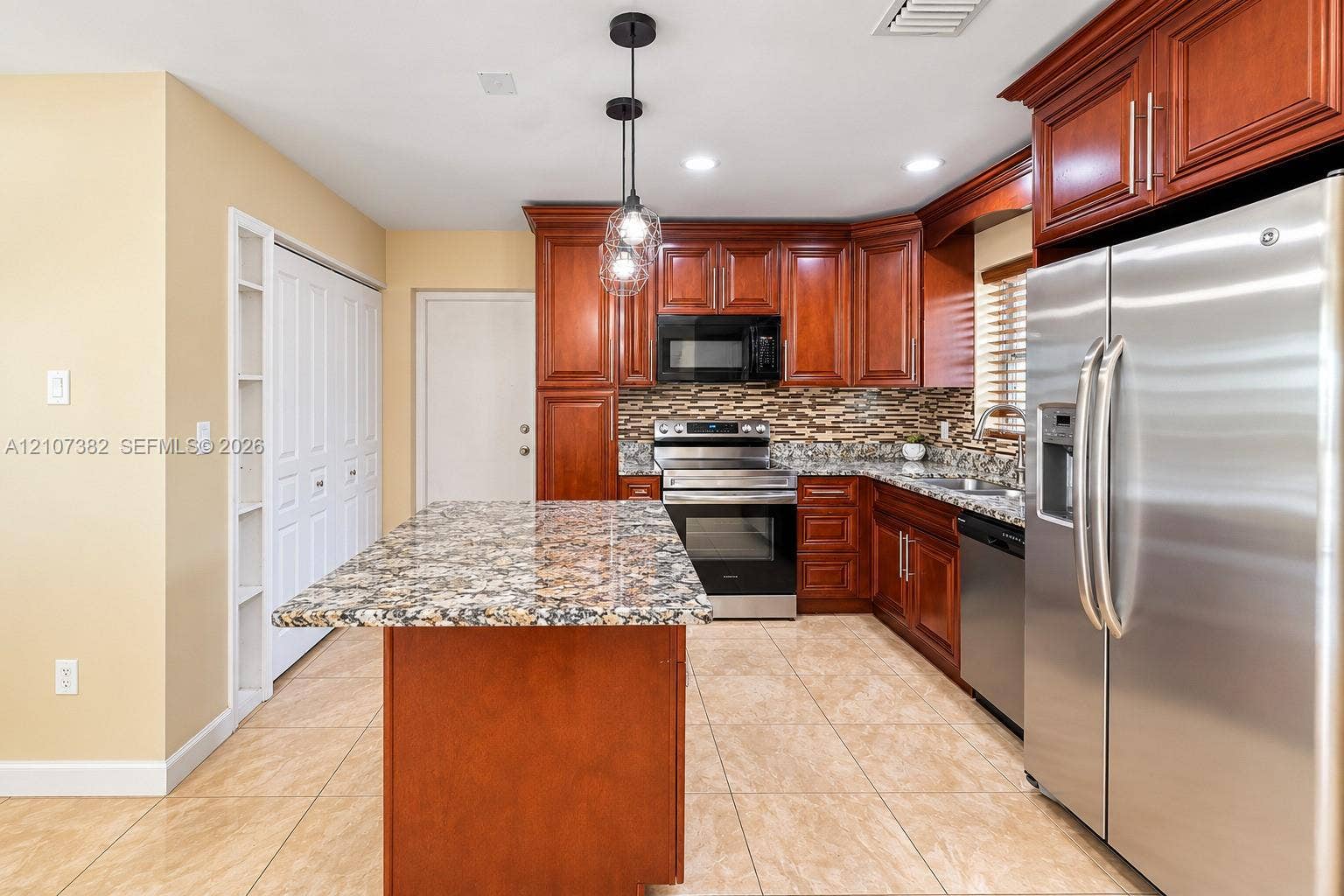 859 Caroline Circle, Palm Beach, FL 33413 Kitchen featuring raised-panel wood cabinetry, stone countertops, stainless steel appliances, multi-toned stone tile backsplash, and ceramic tile flooring