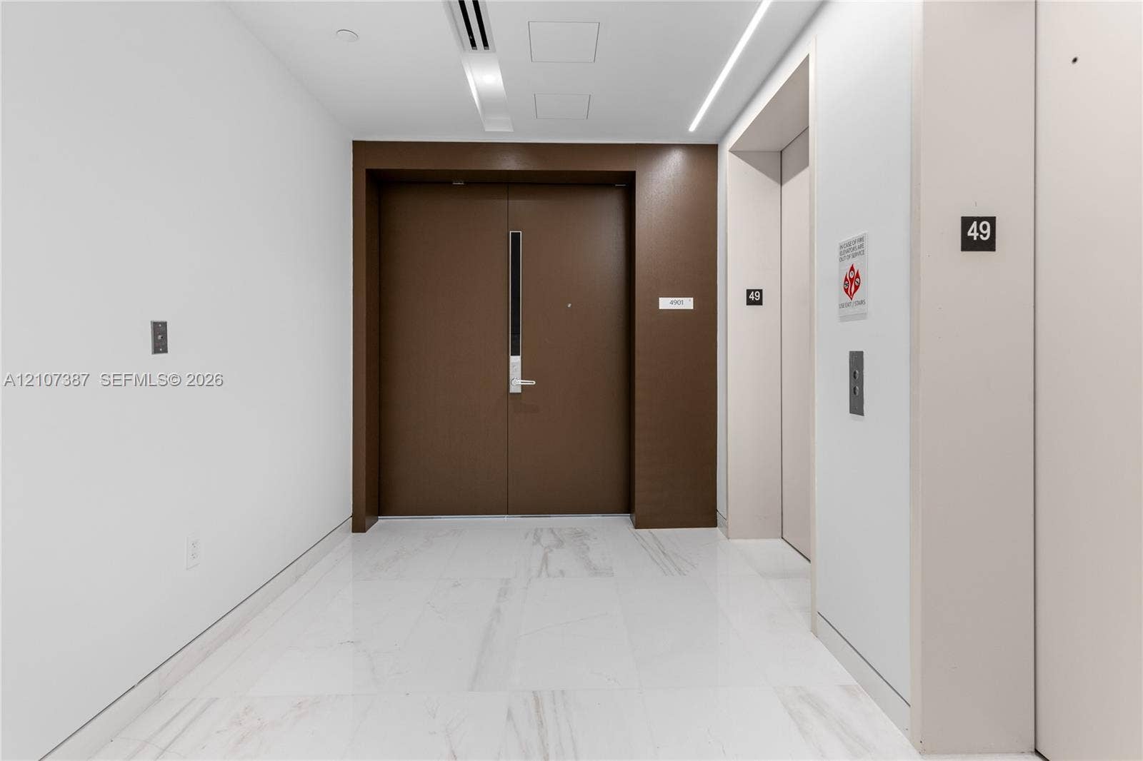 Entry foyer featuring white stone-finish flooring, double solid-core doors, and recessed linear ceiling lighting