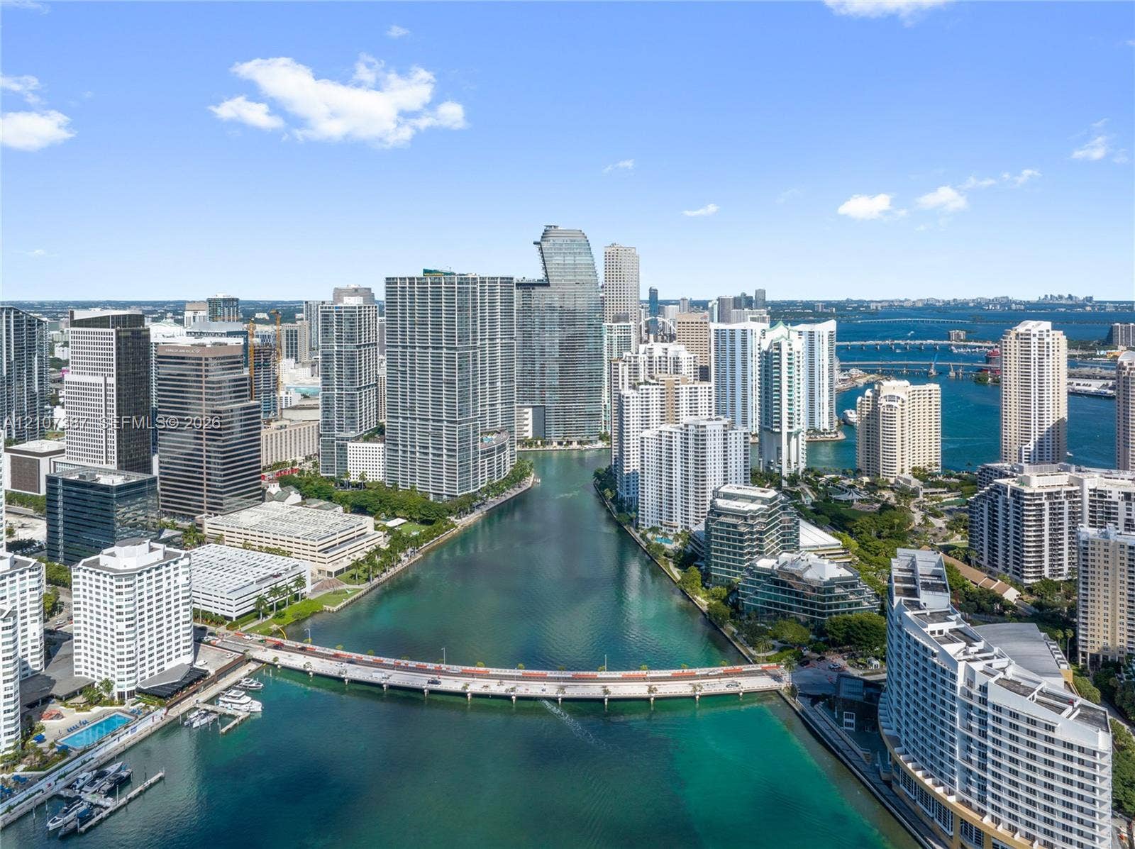 Aerial perspective featuring urban high-rise skyline, waterfront access, marina, and city bridge infrastructure