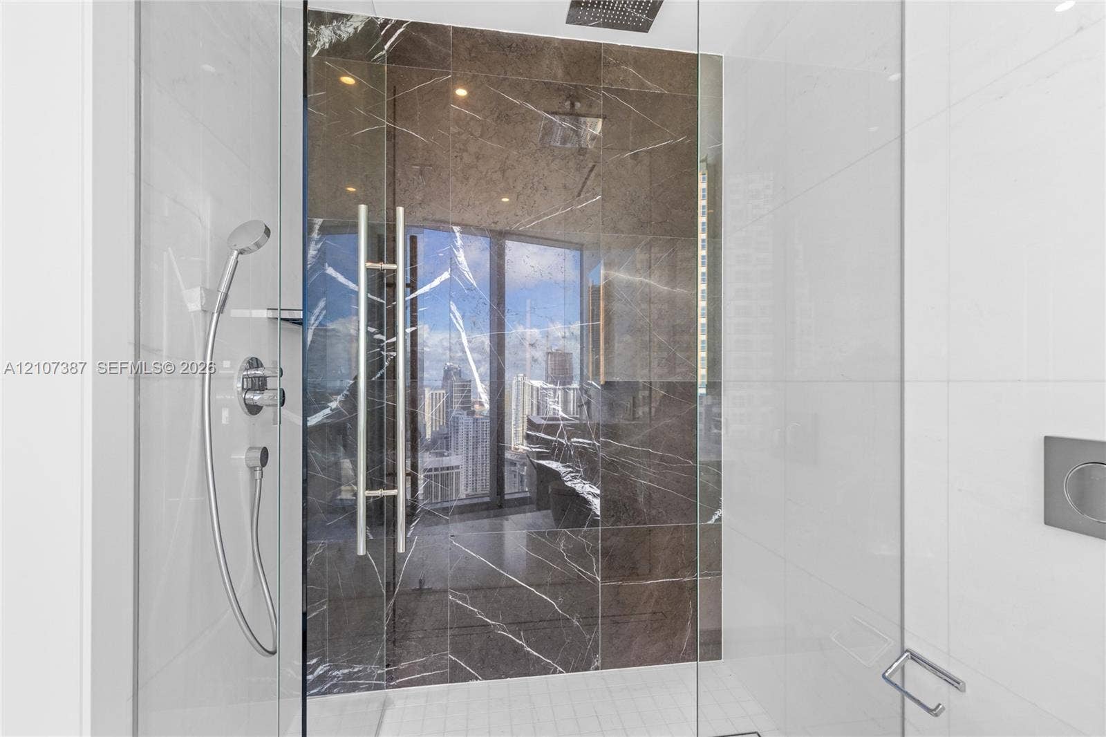 Walk-in shower featuring large-format dark stone tile accent wall, glass enclosure, ceiling-mounted rainfall showerhead, and integrated chrome handheld sprayer