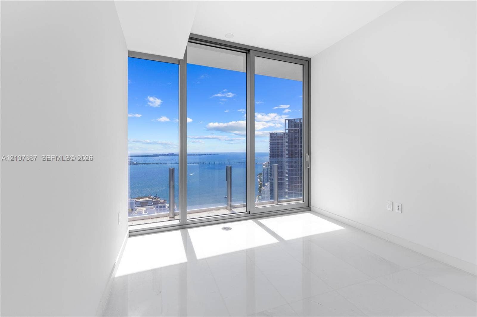 Floor-to-ceiling sliding glass doors, polished tile flooring, and integrated balcony with glass railing showcasing maritime and urban scenery