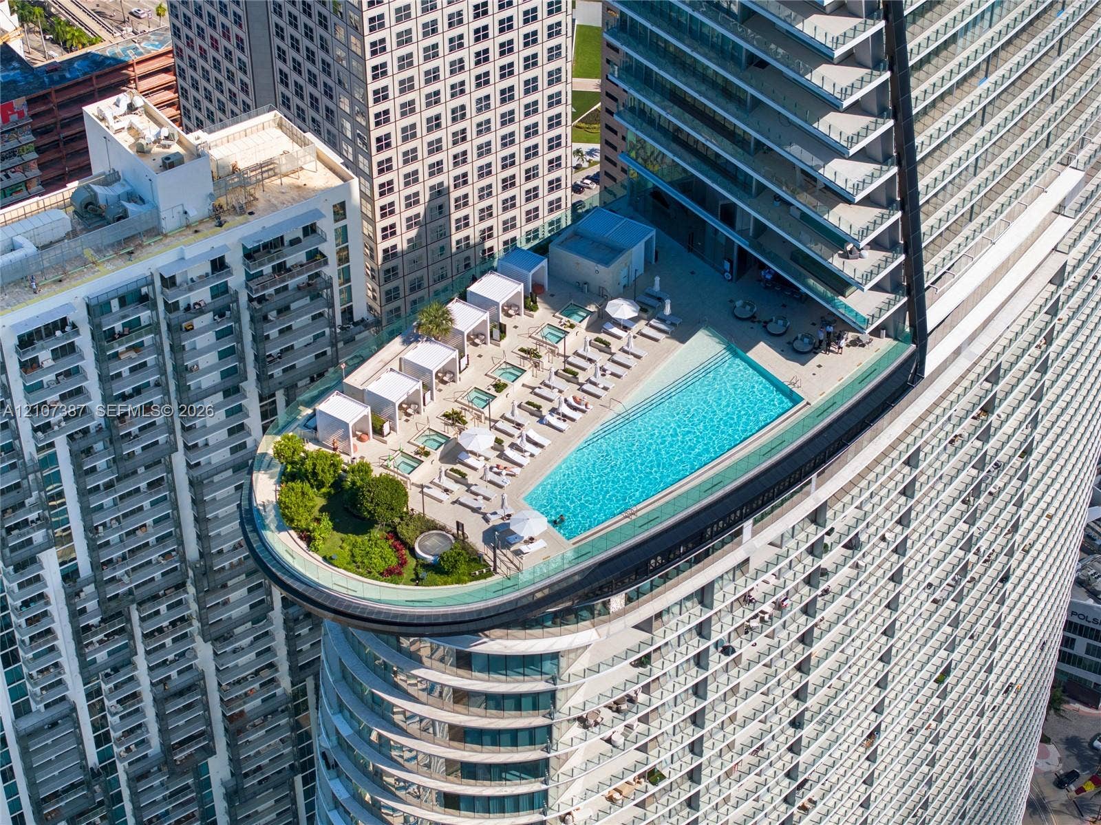 Rooftop terrace featuring an infinity-edge pool, integrated hot tubs, structured cabanas, glass railings, and landscaped green space