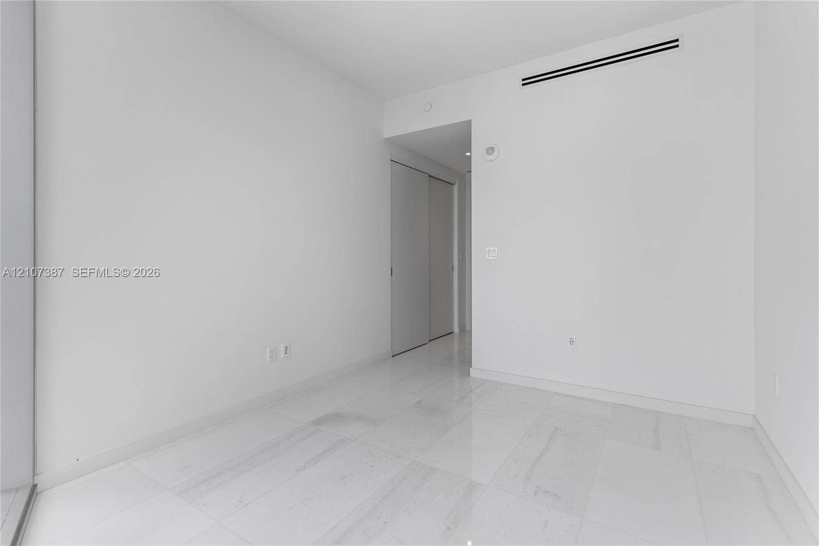 Minimalist interior space featuring polished light-toned stone flooring and dual-panel sliding closet doors