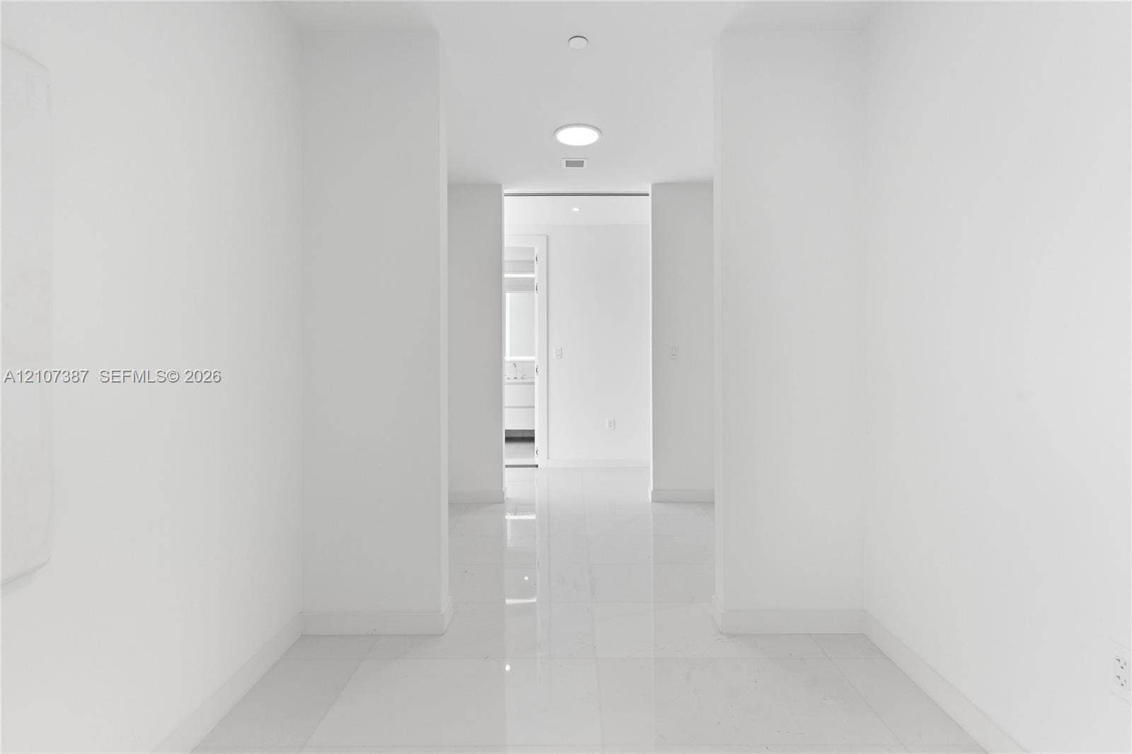 Interior corridor featuring polished stone-finish tile flooring, clean white walls, and recessed ceiling lighting