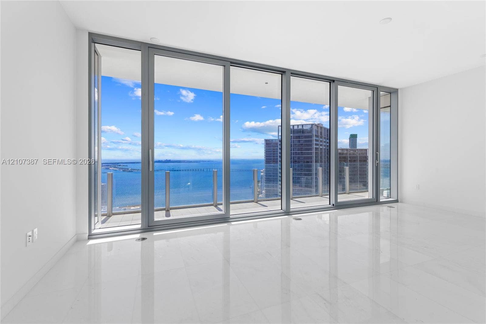 Floor-to-ceiling glass panel walls, expansive terrace with glass railing, large-format polished tile flooring, and panoramic water and city scenery