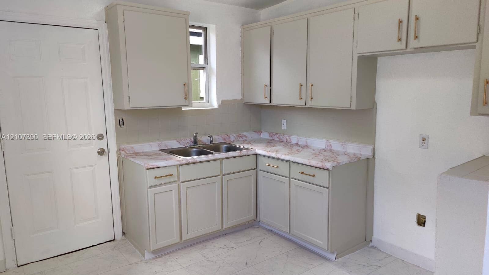 Kitchen area featuring shaker-style cabinetry, stone-patterned countertops, a dual-basin stainless steel sink with a high-arch faucet, and light-toned tile flooring