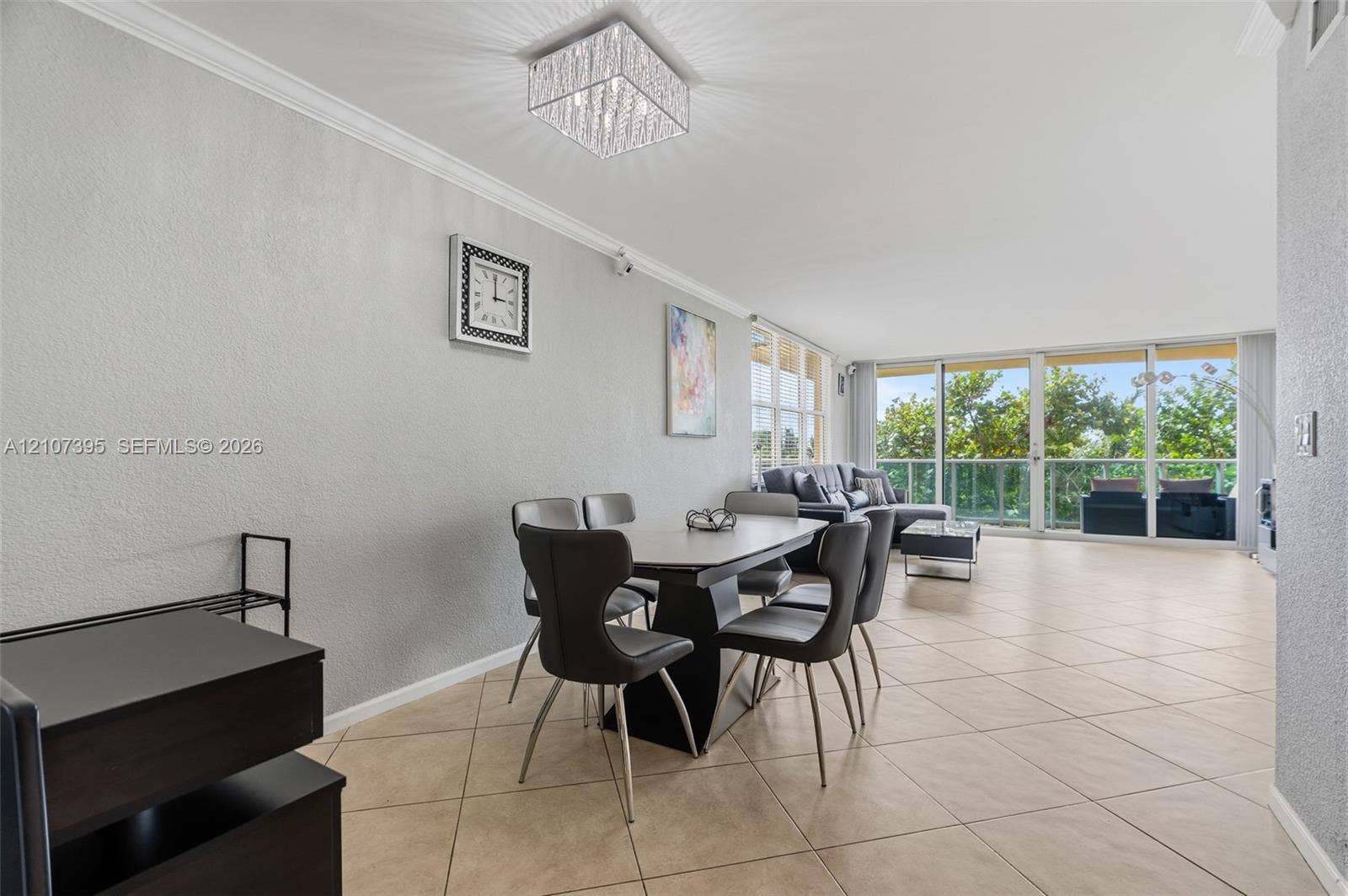 Open-concept interior featuring large-format tile flooring, crown molding, a crystal-accented flush mount light fixture, and floor-to-ceiling glass sliding doors with access to an exterior balcony