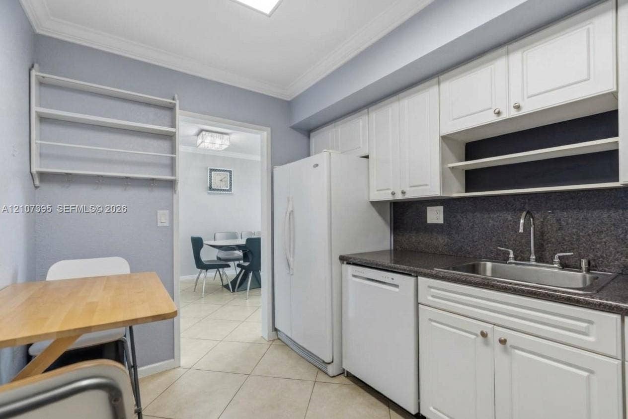 Kitchen featuring white raised-panel cabinetry, dark stone-finish countertops, stainless steel sink with gooseneck faucet, tile flooring, and built-in wall shelving