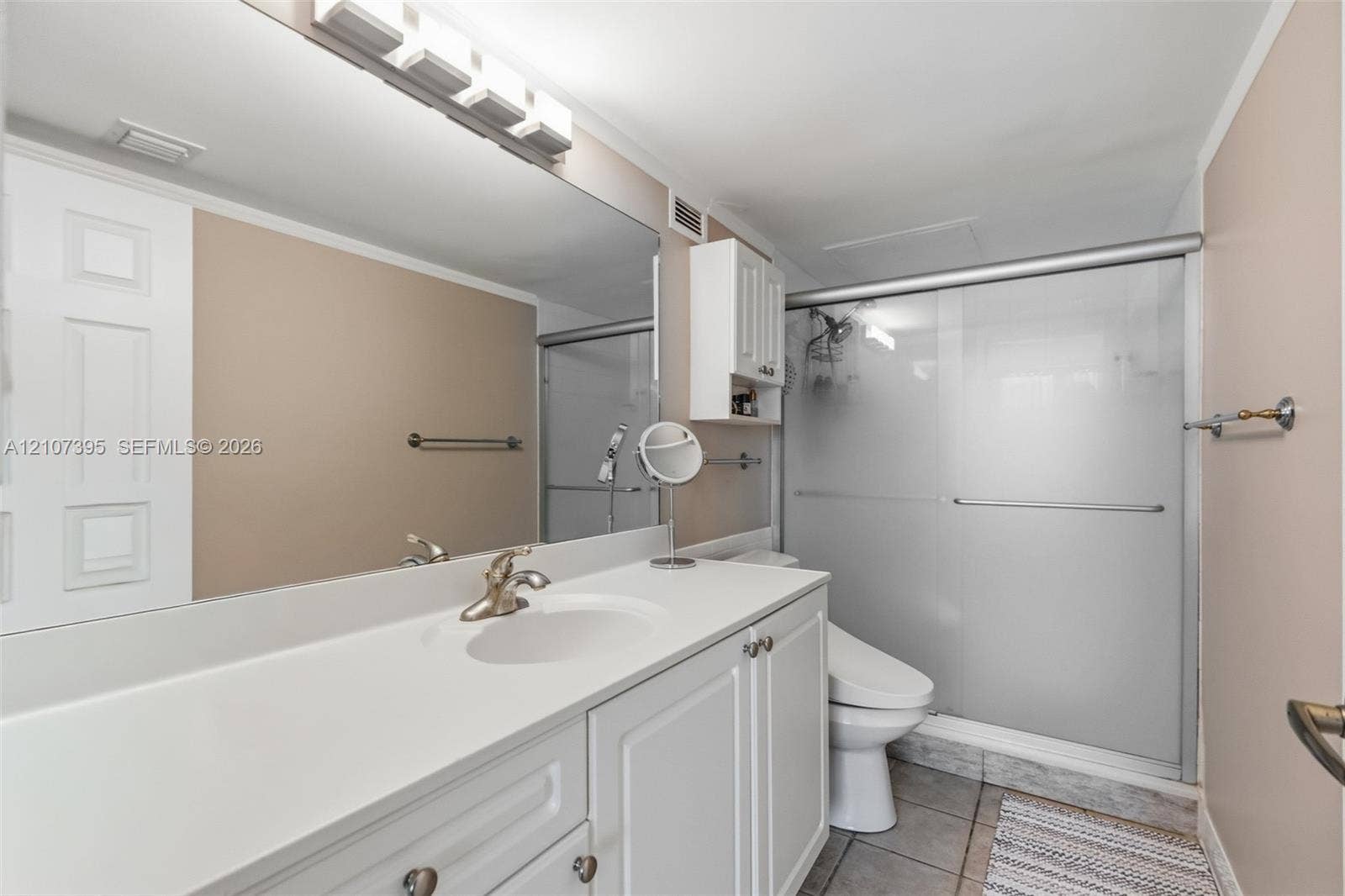 Bathroom featuring a white vanity with an integrated basin, a full-width wall mirror, an overhead multi-light fixture, built-in upper cabinetry, and a walk-in shower with frosted sliding glass doors