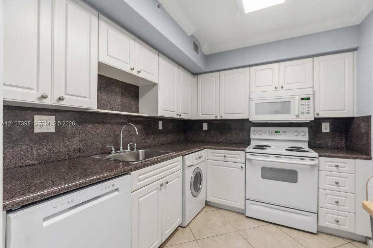 Kitchen featuring white cabinetry, stone countertops, integrated dishwasher, built-in microwave, and tile flooring