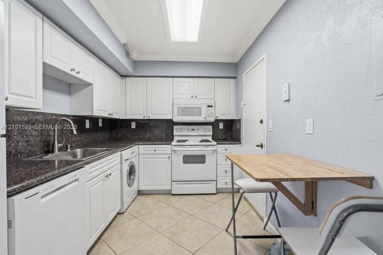 Kitchen featuring white cabinetry, dark stone-finish countertops, tile flooring, integrated appliances, and a mounted drop-leaf table