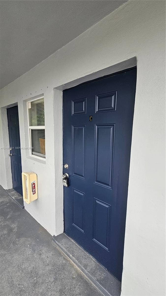 1524 SW 5th Place, #C, Fort Lauderdale, Fort Lauderdale, FL 33312 Exterior entrance featuring a navy blue six-panel door, a single-hung window with horizontal blinds, and a mounted fire extinguisher cabinet