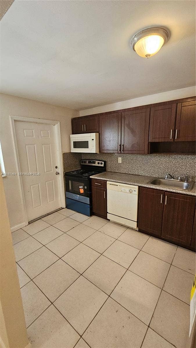 1524 SW 5th Place, #C, Fort Lauderdale, Fort Lauderdale, FL 33312 Kitchen featuring dark wood-finish cabinetry, stone-texture countertops, tile flooring, and integrated white appliances