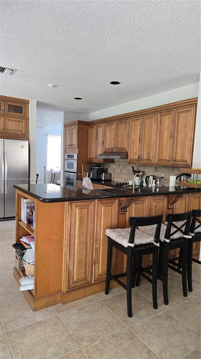 1559 Elm Grove Road, Weston, Weston, FL 33327 Kitchen featuring natural wood cabinetry, polished stone countertops, stainless steel wall-mounted oven, and built-in shelving integrated into the peninsula