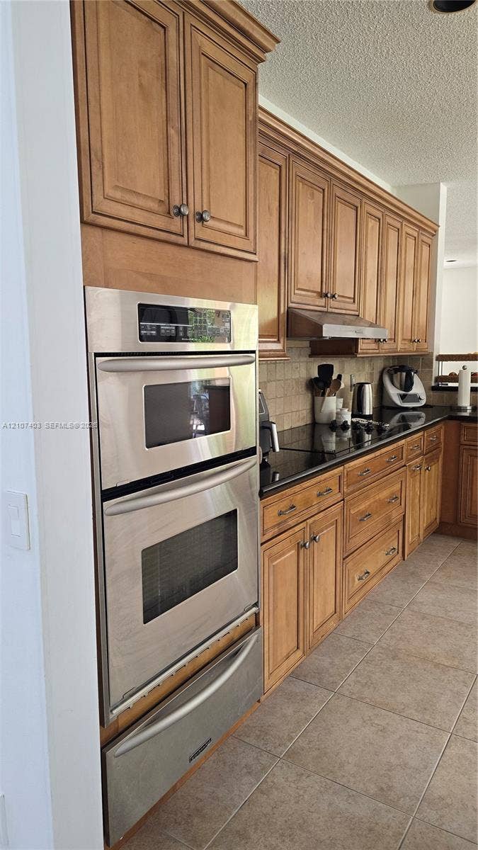 1559 Elm Grove Road, Weston, Weston, FL 33327 Kitchen featuring natural-finish wood cabinetry, dark stone countertops, tile backsplash, and built-in stainless steel double wall ovens