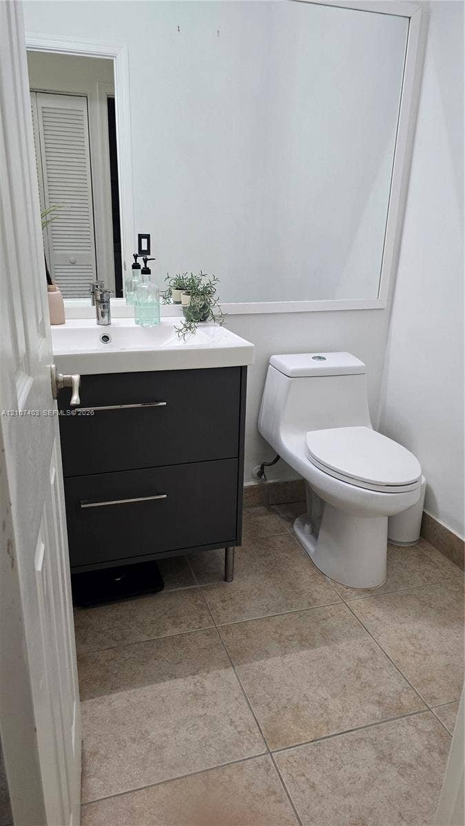 1559 Elm Grove Road, Weston, Weston, FL 33327 Dark gray dual-drawer vanity with a white countertop, rectangular integrated basin, one-piece toilet, large wall-mounted mirror, and tile flooring