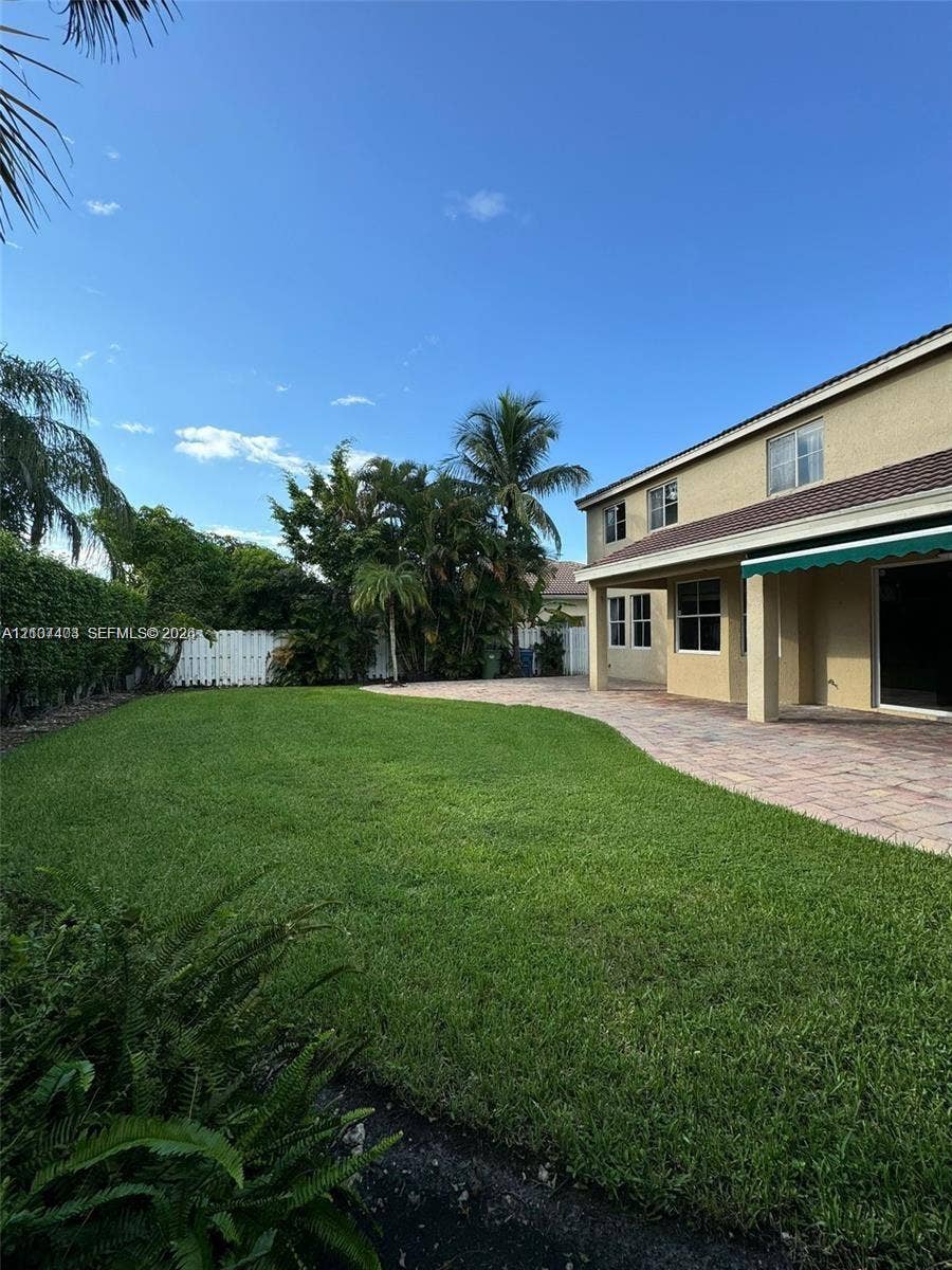 1559 Elm Grove Road, Weston, Weston, FL 33327 Expansive backyard featuring a manicured lawn, paver patio, attached retractable awning, and perimeter privacy fencing