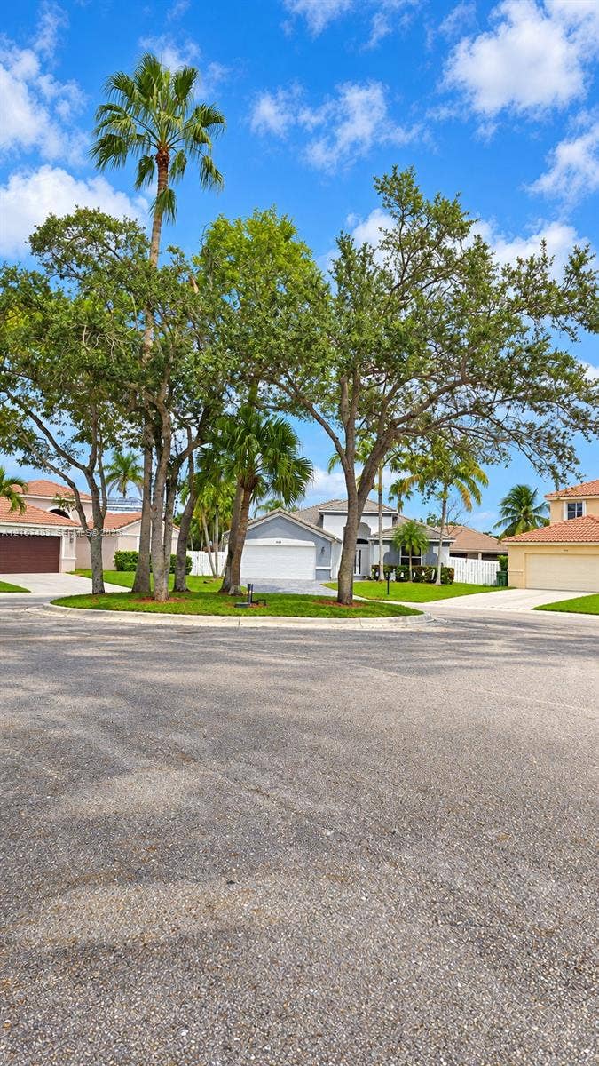 1559 Elm Grove Road, Weston, Weston, FL 33327 Exterior profile featuring a concrete tile roof, light-toned stucco facade, paved driveway, and mature landscaping with palm trees