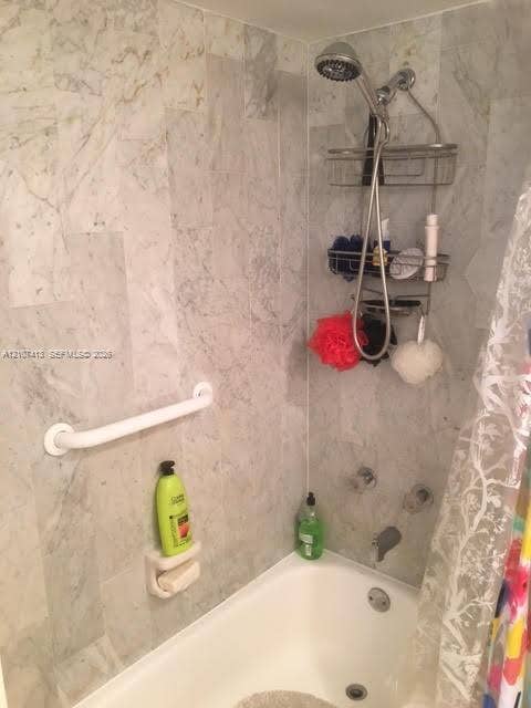 2301 S Ocean Drive, #1606, Hollywood, Hollywood, FL 33019 Shower enclosure featuring stone-tiled walls, a built-in soap dish, a wall-mounted grab bar, and a chrome-finish shower fixture