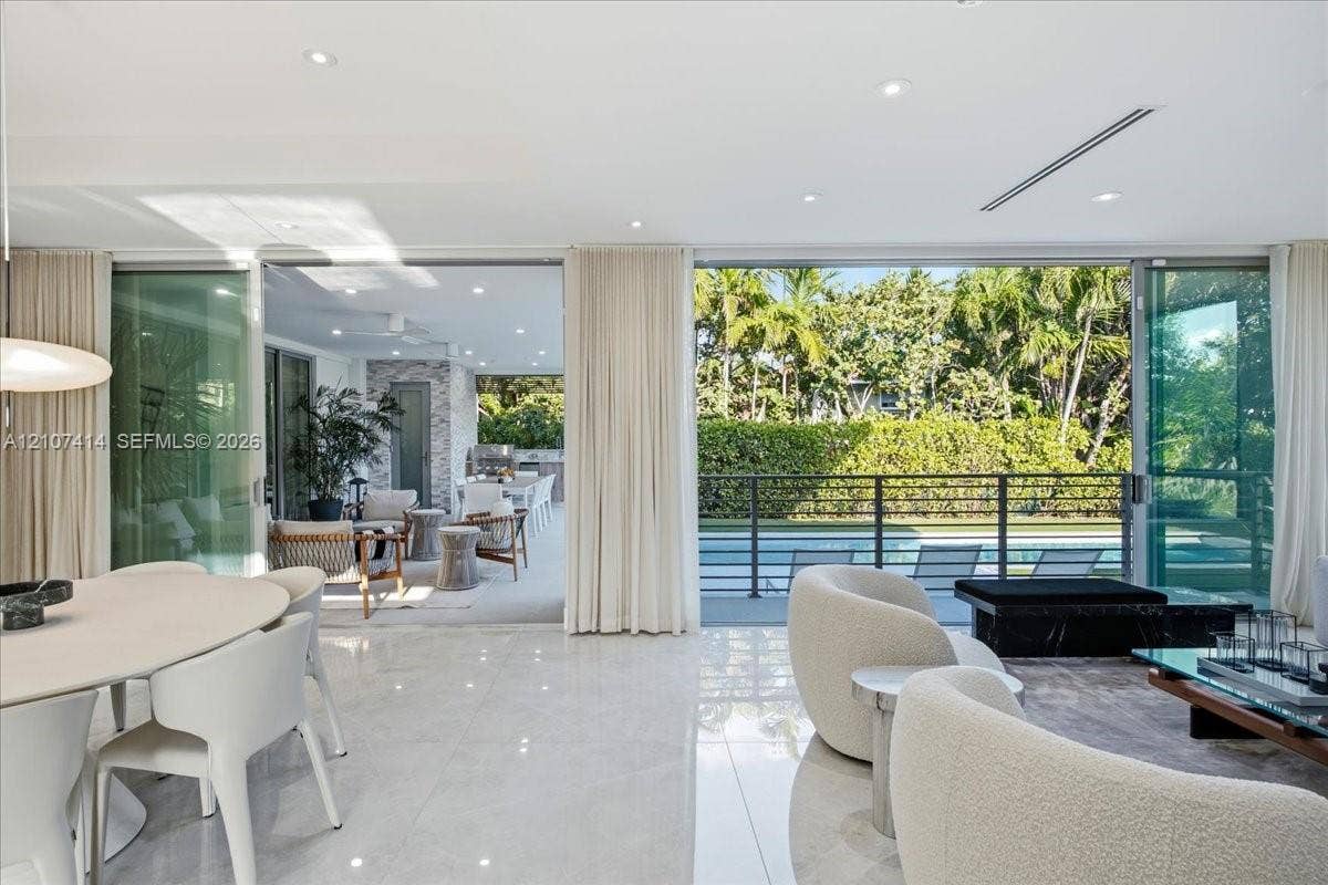 Open-concept interior featuring large-format stone flooring, floor-to-ceiling glass sliding doors, recessed lighting, and a covered outdoor patio