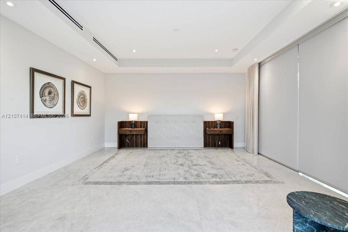 Tray ceiling with recessed lighting, large-format tile flooring, built-in wooden nightstands, and expansive wall-to-wall sliding door panels