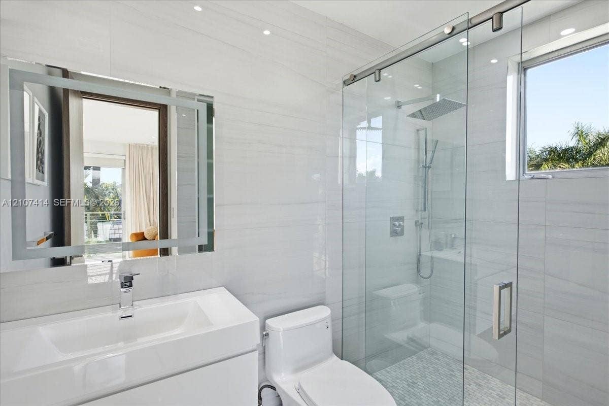 Bathroom featuring white tile wall cladding, a floating vanity with an integrated sink, an LED-illuminated mirror, a walk-in shower with a glass sliding enclosure, and recessed lighting