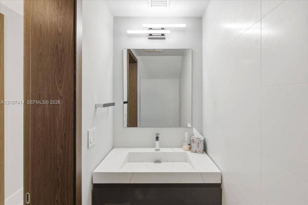 Floating vanity with an integrated basin, quartz countertop, minimalist wall-mounted lighting, frameless mirror, and large-format wall tile