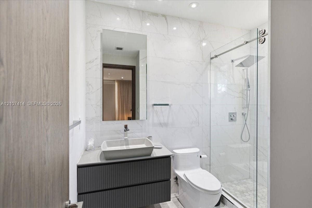 Floating vanity with a vessel sink, full-height tile wall, frameless glass shower enclosure, rainfall showerhead, and recessed lighting