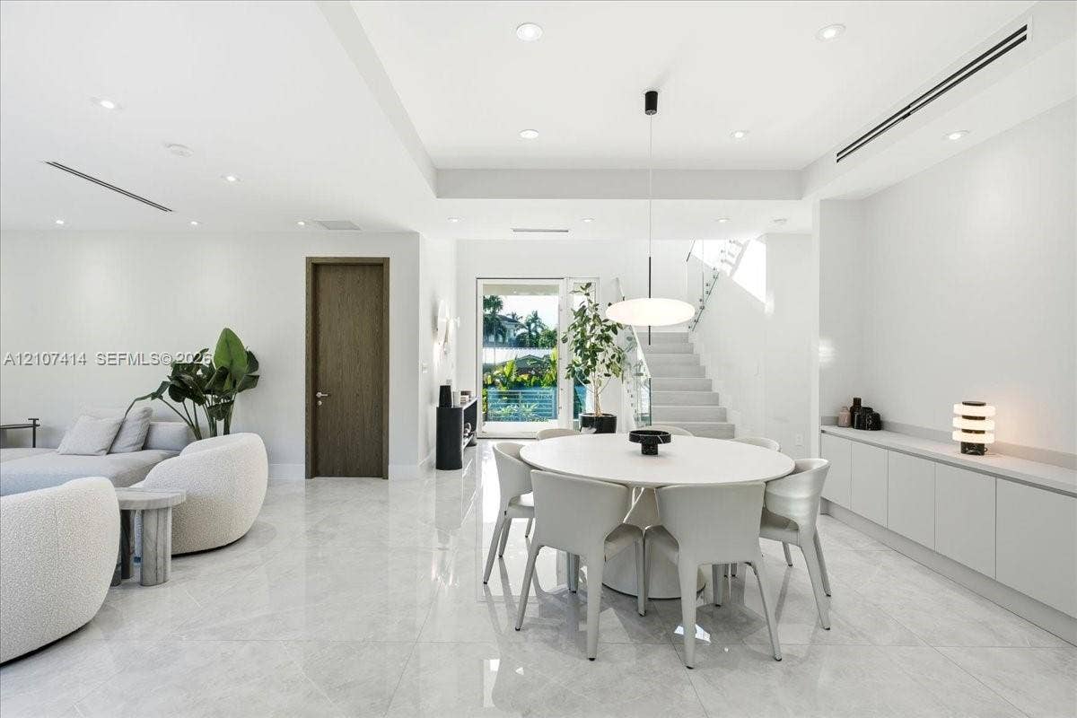 Open-concept interior featuring large-format polished stone flooring, recessed LED lighting, built-in cabinetry with a stone countertop, a modern pendant light fixture, and a staircase with glass railings