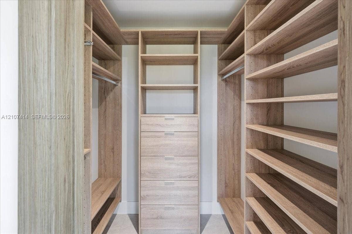 Custom walk-in closet featuring wood-finish cabinetry, built-in shelving, integrated dresser drawers, and metal hanging rods