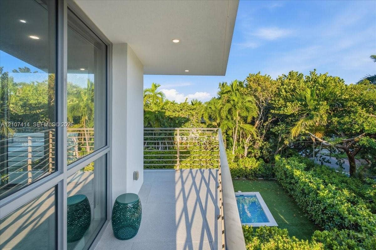 Covered balcony featuring tile flooring, horizontal cable railing, recessed lighting, and floor-to-ceiling glass paneling overlooking a private pool and manicured landscaping