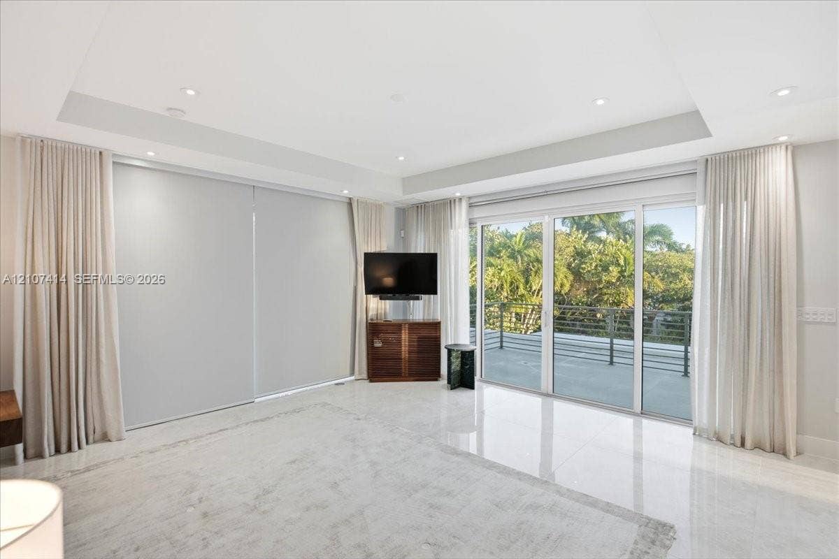 Tray ceiling with recessed lighting, large format tile flooring, and sliding glass doors opening to a balcony with metal railing