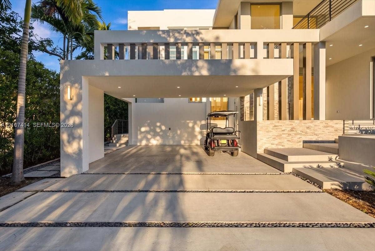 Modern architectural facade featuring a covered porte-cochre, recessed lighting, stacked stone exterior detailing, and a concrete driveway with decorative rock inlay
