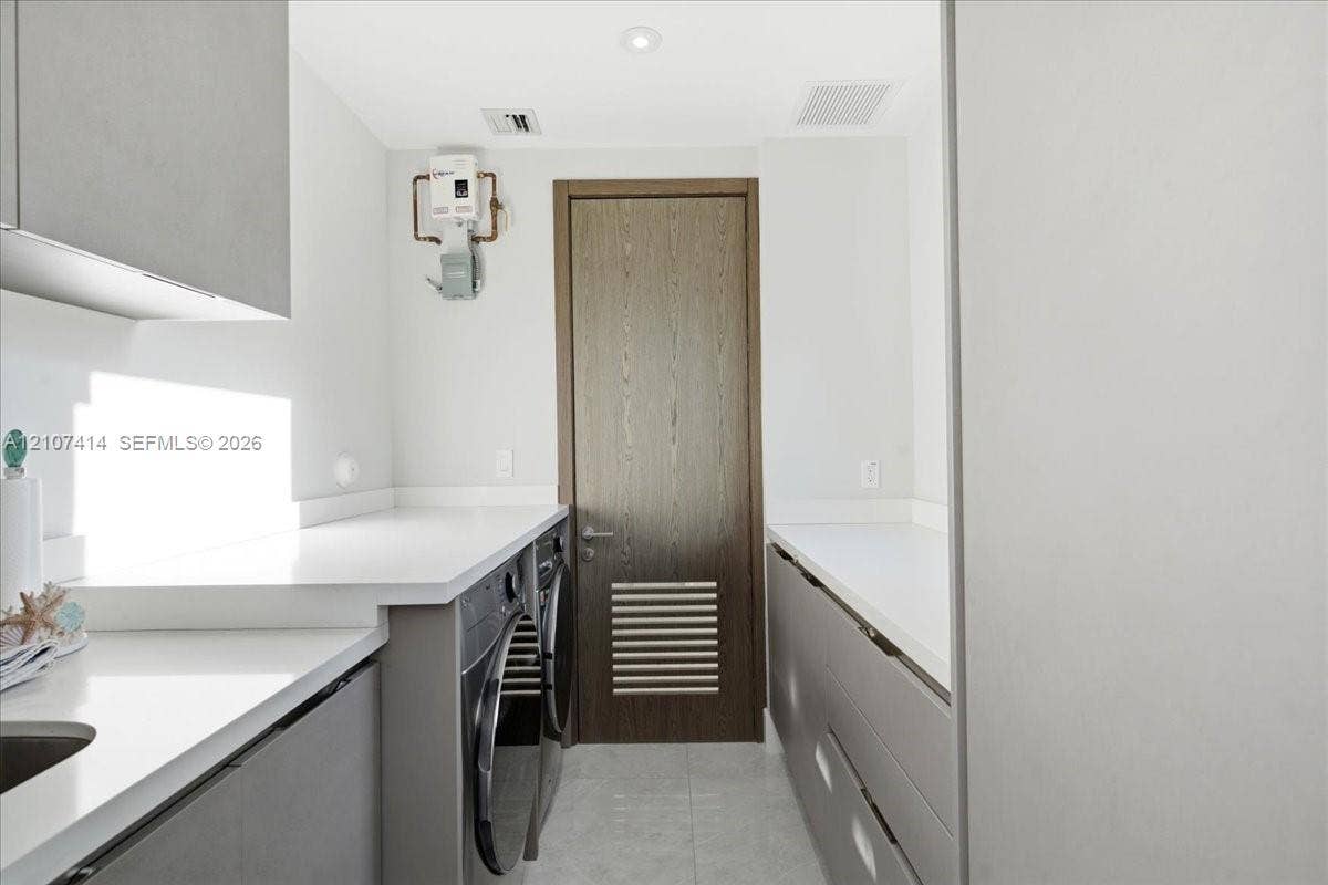 Laundry room featuring grey flat-panel cabinetry, white solid-surface countertops, integrated sink, and wood-finish door with louvered panel