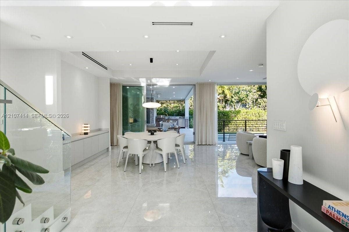 Large-format polished stone flooring, recessed ceiling lighting with tray detail, glass-panel staircase railing, built-in cabinetry, and expansive sliding glass doors