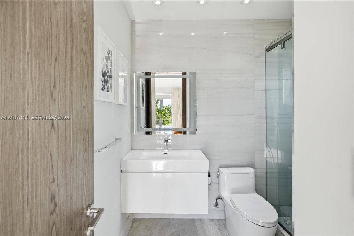 Modern bathroom featuring a white floating vanity with a vessel sink, integrated LED-lit mirror, glass-enclosed shower, and stone-finish floor tiling