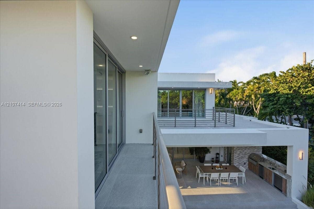Modern architectural exterior featuring expansive covered balconies, metal railings, recessed lighting, and a ground-level outdoor kitchen with stone veneer detailing